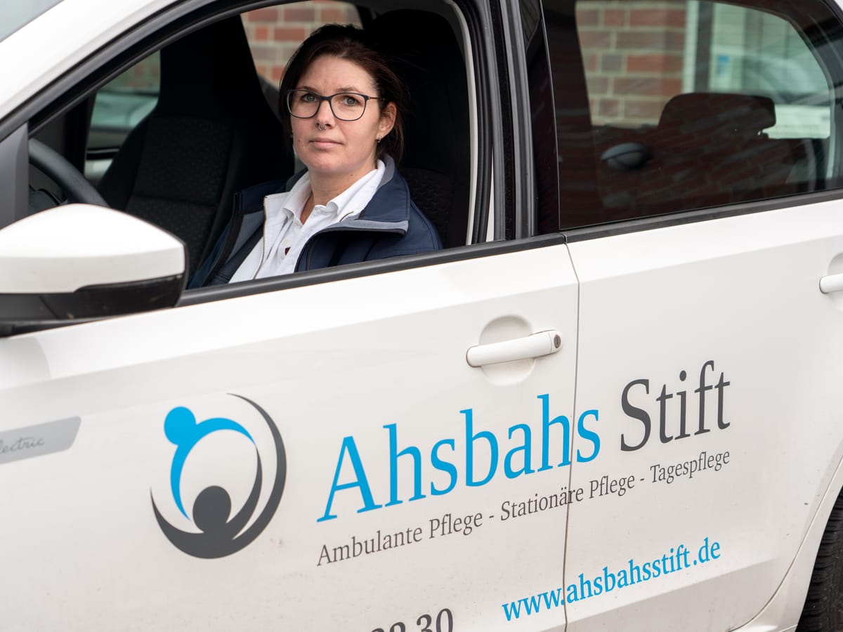 Eine Pflegerin sitzt am Steuer eines weißen Dienstwagens mit dem Logo des Ahsbahs Stift.