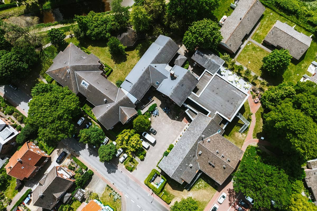 Luftaufnahme der Anlage: Gebäude mit grauen Dächern zwischen Bäumen und Gärten.
