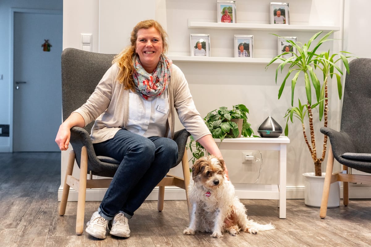 Eine Mitarbeiterin sitzt lachend im Sessel, neben ihr ein kleiner Hund.