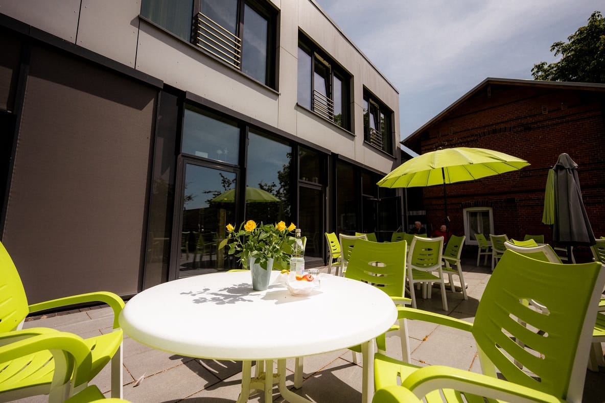 Sonnige Terrasse mit runden Tischen, hellgrünen Stühlen und Sonnenschirmen.