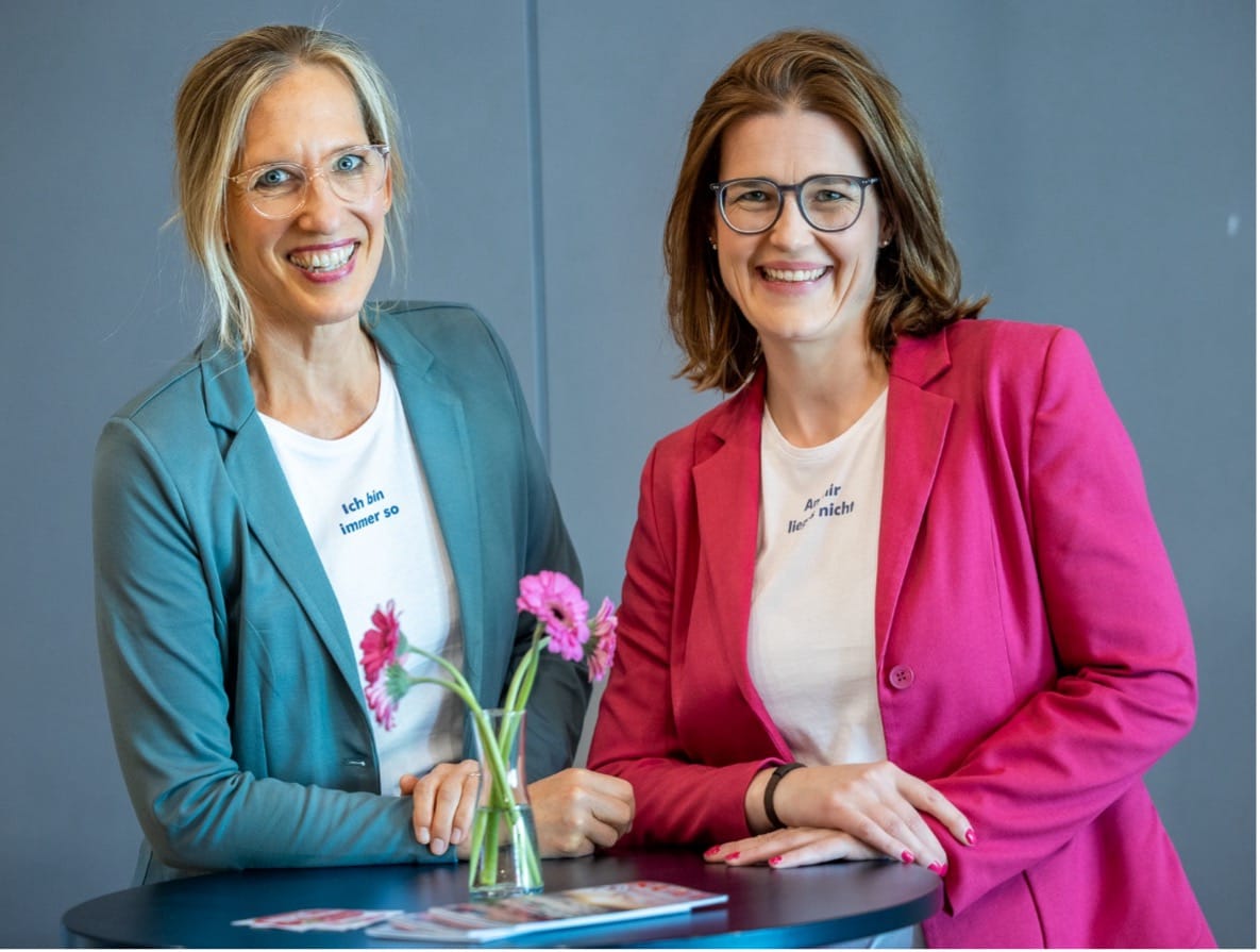 Zwei Frauen stehen lachend an einem Stehtisch mit Gerbera.